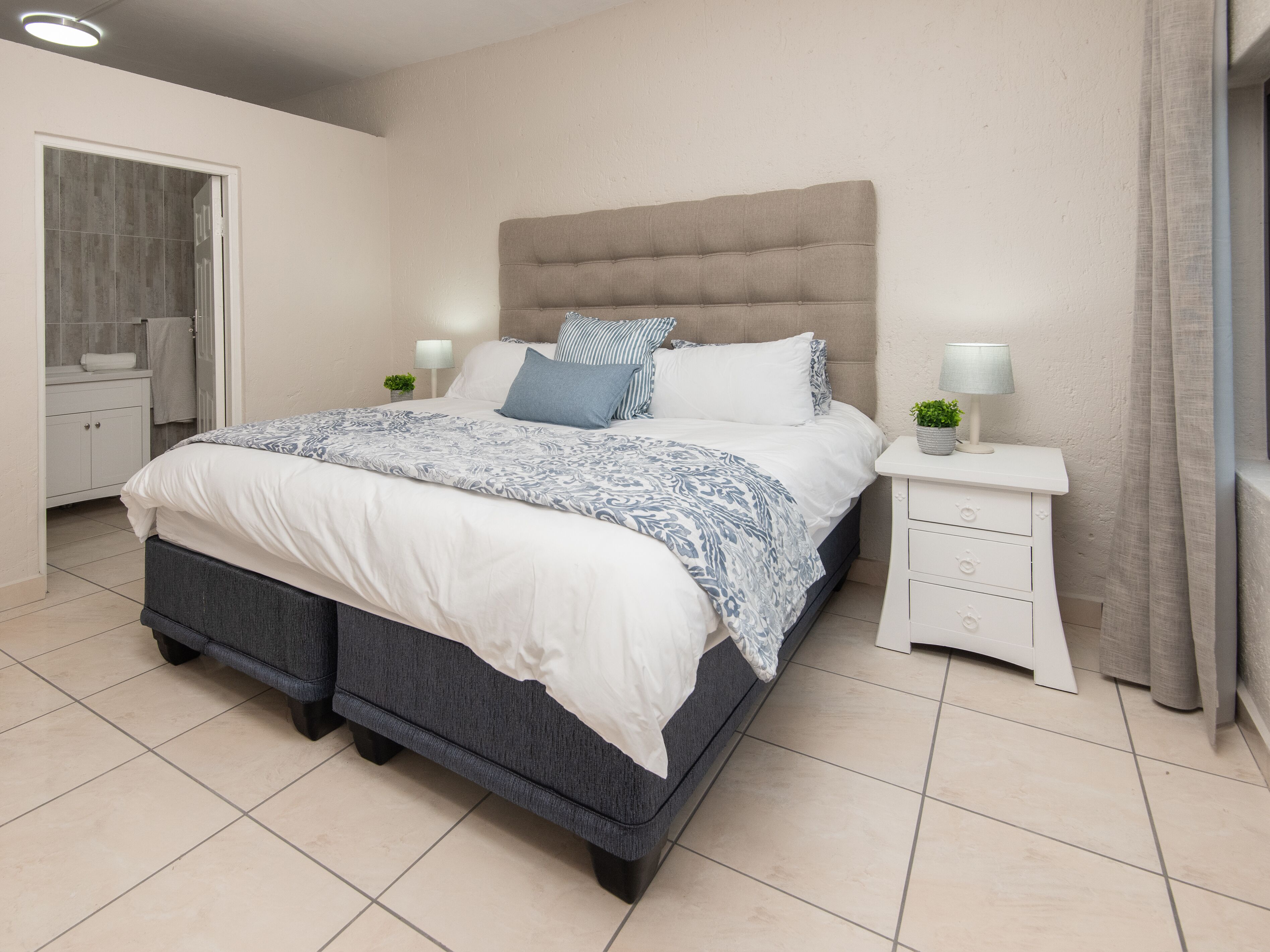 A bedroom with a bed, nightstands, a dresser, and a window with curtains.