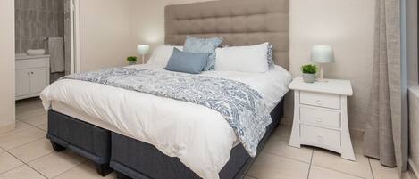 A bedroom with a bed, nightstands, a dresser, and a window with curtains.