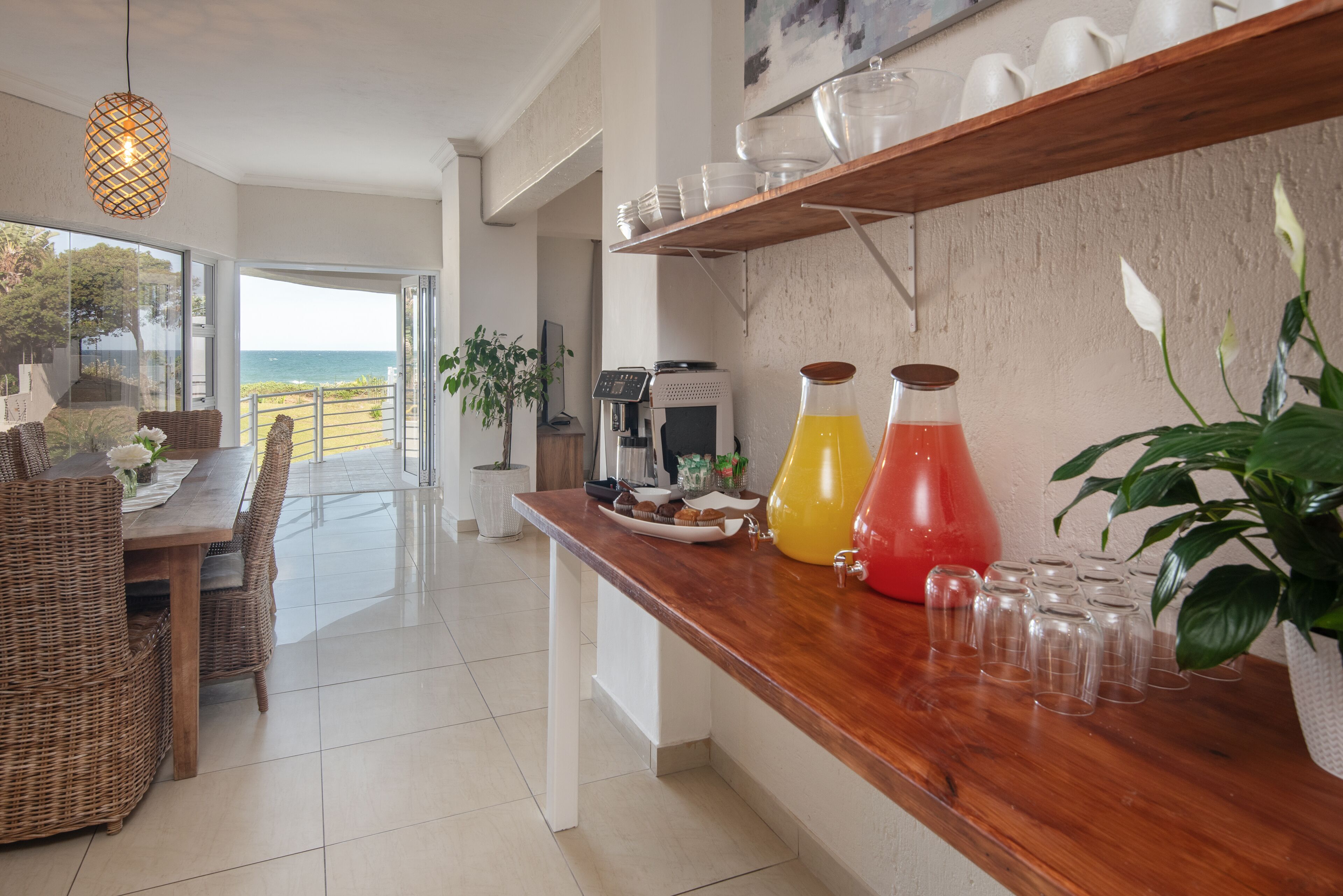 Una cocina moderna con encimera de madera, una zona de comedor con mobiliario de mimbre y vistas al mar a través de amplios ventanales.