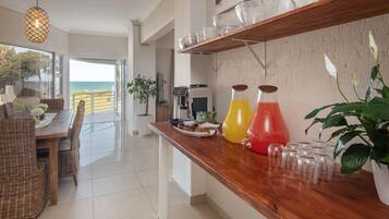Una cocina moderna con encimera de madera, una zona de comedor con mobiliario de mimbre y vistas al mar a través de amplios ventanales.