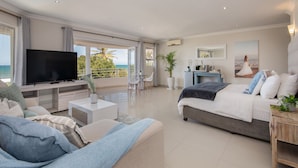 Un dormitorio moderno con una cama grande, un televisor y un balcón con vistas al océano.