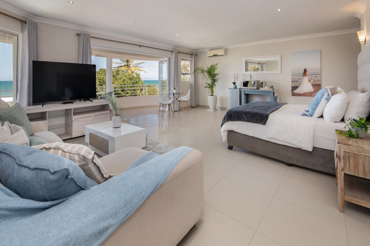 Quarto moderno com cama grande, TV e varanda com vista para o oceano.