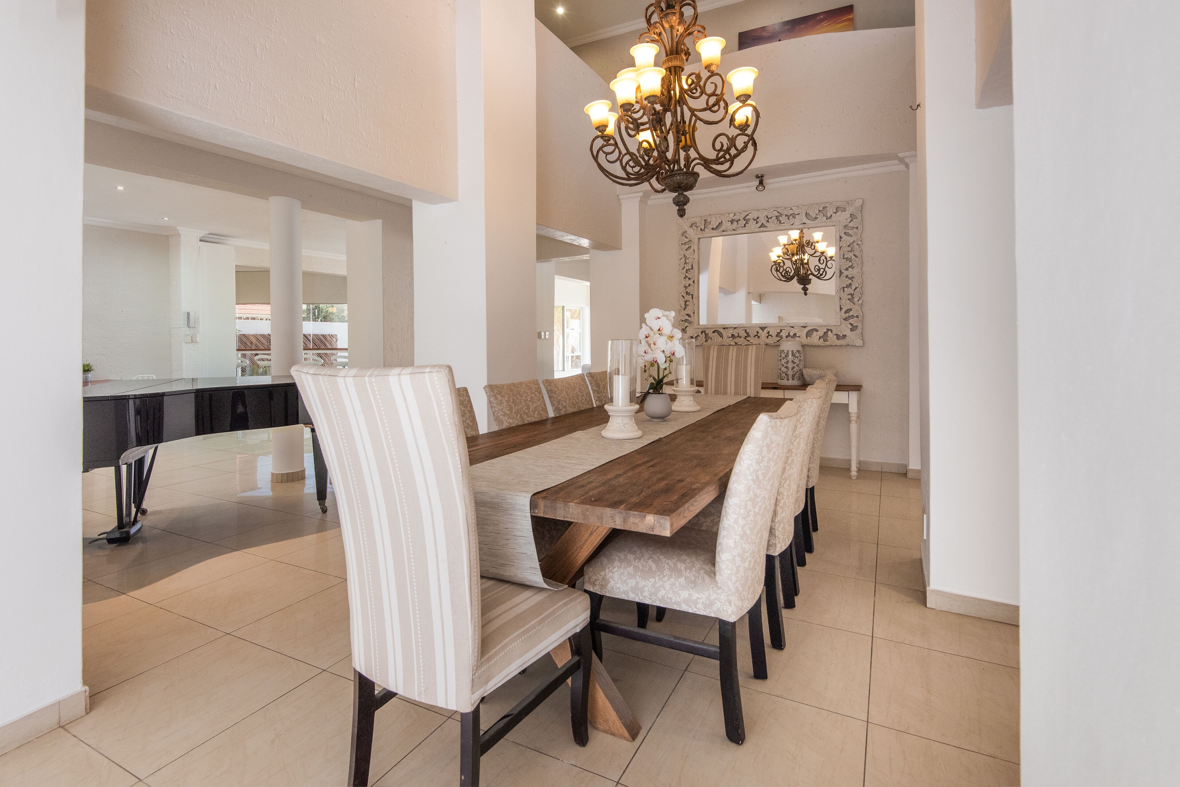 A spacious dining area with a long wooden table, upholstered chairs, and a decorative chandelier.