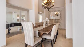 A spacious dining area with a long wooden table, upholstered chairs, and a decorative chandelier.