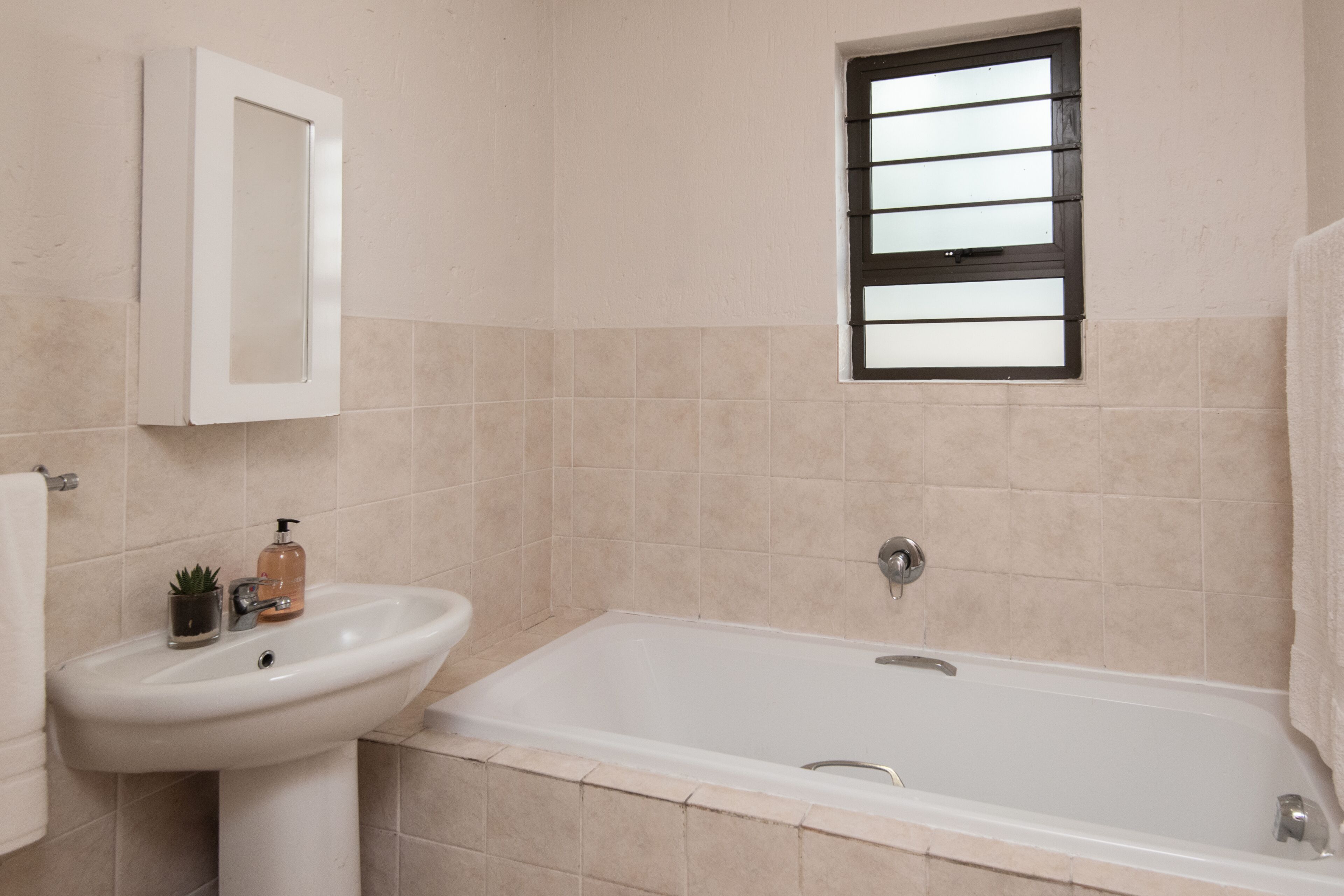 A bathroom with a sink, a mirror, a window, and a bathtub.