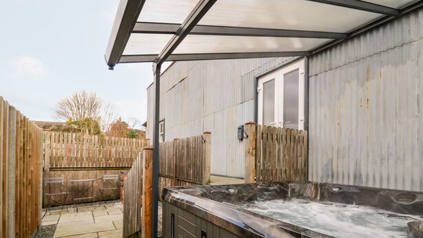 Un área de hidromasaje con valla de madera, un patio cubierto y un muro de metal.