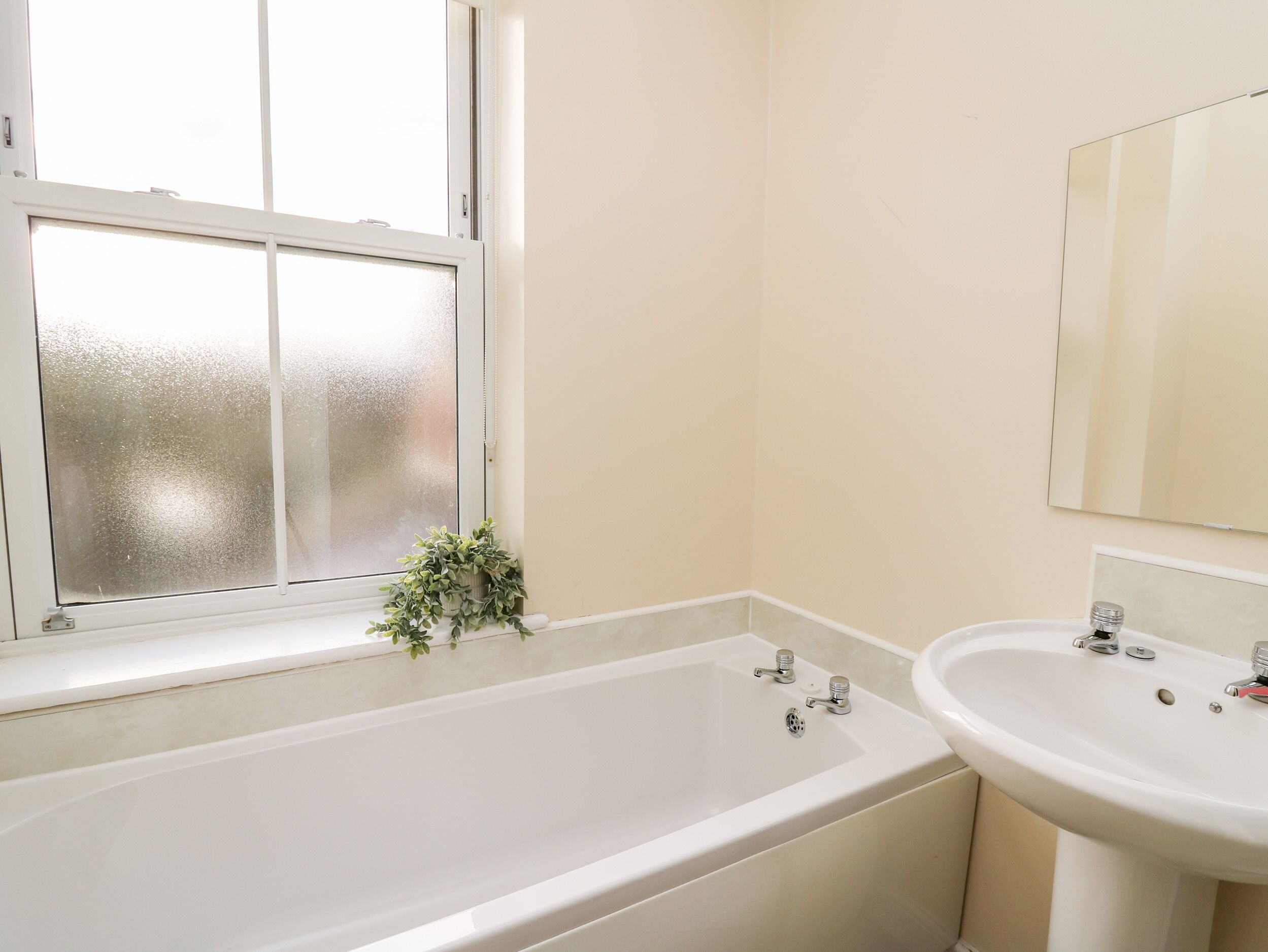 A bathroom with a bathtub, a sink, and a window with frosted glass.