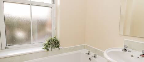 A bathroom with a bathtub, a sink, and a window with frosted glass.