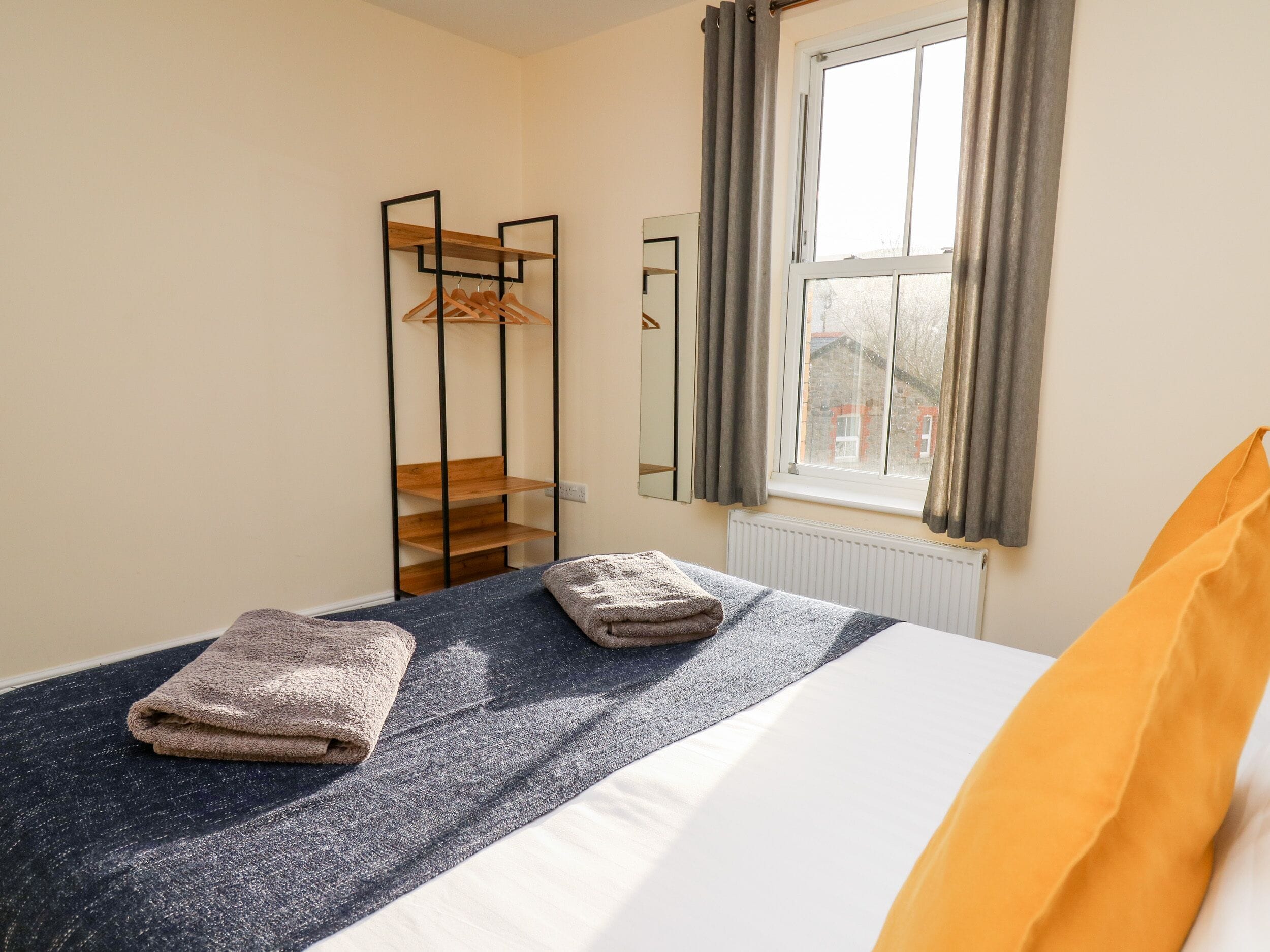 Un dormitorio con cama, un armario de madera, un espejo y una ventana con cortinas.