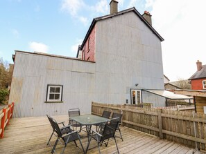 A building with a corrugated metal exterior, a wooden deck, and a table with chairs. - Afonwy House (Rhayader)