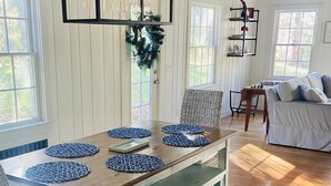 Un comedor con una mesa de madera, manteles individuales azules, sillas de mimbre y una lámpara colgante.
