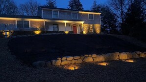 Una casa de dos pisos con un muro de contención de piedra y un jardín ajardinado.