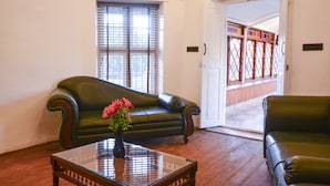 Une pièce avec un canapé en cuir vert, une table basse en verre ornée d’un vase de fleurs, un plancher en bois et une porte donnant sur un balcon doté d’une balustrade en bois.