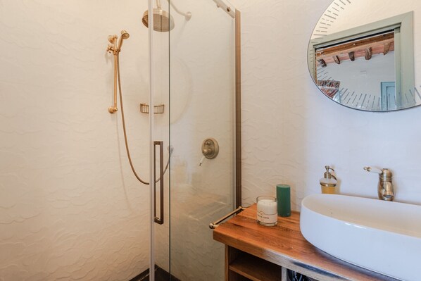 A bathroom with a glass-enclosed shower, a wooden vanity with a sink, and a mirror above the vanity.