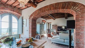 A spacious living area with a wooden dining table set for a meal, a comfortable sofa, and a television. - Villa Alice, panoramic stone farmhouse to sleep 10 with pool in Lucca (Lucca)
