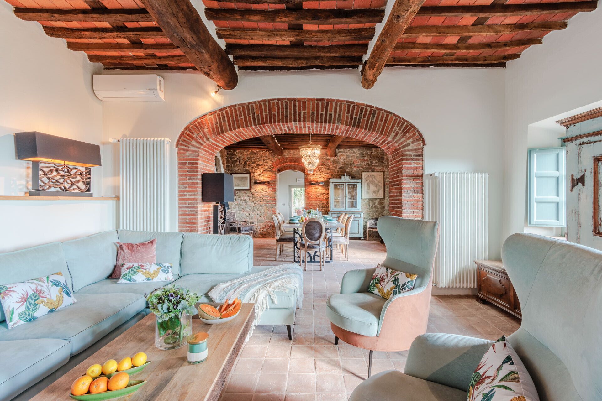 A spacious living area with a high ceiling, exposed brick walls, and a dining area with a table and chairs.