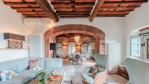A spacious living area with a high ceiling, exposed brick walls, and a dining area with a table and chairs. - Villa Alice, panoramic stone farmhouse to sleep 10 with pool in Lucca (Lucca)
