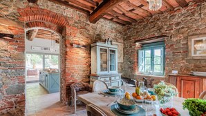 A rustic dining area with a stone wall, wooden beams, and a table set with plates, glasses, and a fruit bowl. - Villa Alice, panoramic stone farmhouse to sleep 10 with pool in Lucca (Lucca)