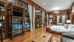Ein geräumiges Zimmer mit Holzboden, einem Bett mit weißer Bettwäsche, einem Couchtisch und Blick auf ein Außenbecken durch große Glasüren.