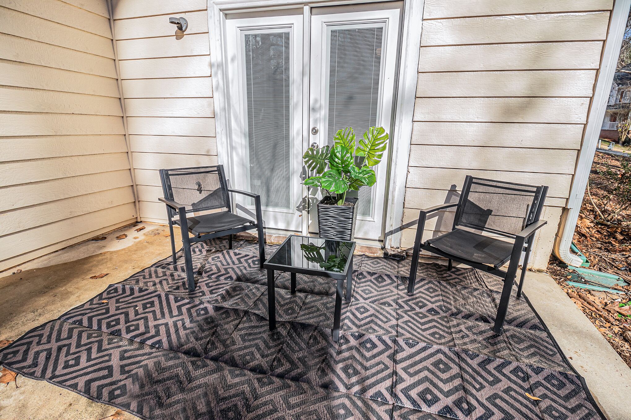 Een terras met twee stoelen, een tafel, een bloempot en een deur met raam.