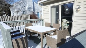 En overdækket terrasse med bord og stole, en træterrasse og en skydedør i glas.