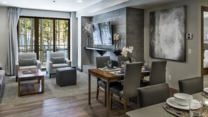 A modern living room with a dining area, large windows, and a flat-screen TV mounted on the wall. - PEAK 8 SKI IN / SKI OUT 2BD/2BA at GRAND COLORADO. SLEEPS UP TO 8. (Breckenridge)