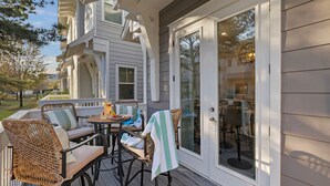 A covered outdoor seating area with wicker furniture and a glass door leading to a patio. - 🌅 Sunset Palms | Golf Cart, Retro Game Room & Walk to The Big Chill (Inlet Bech)