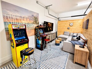 A room with arcade games, a sofa, a TV, and a wooden wall.