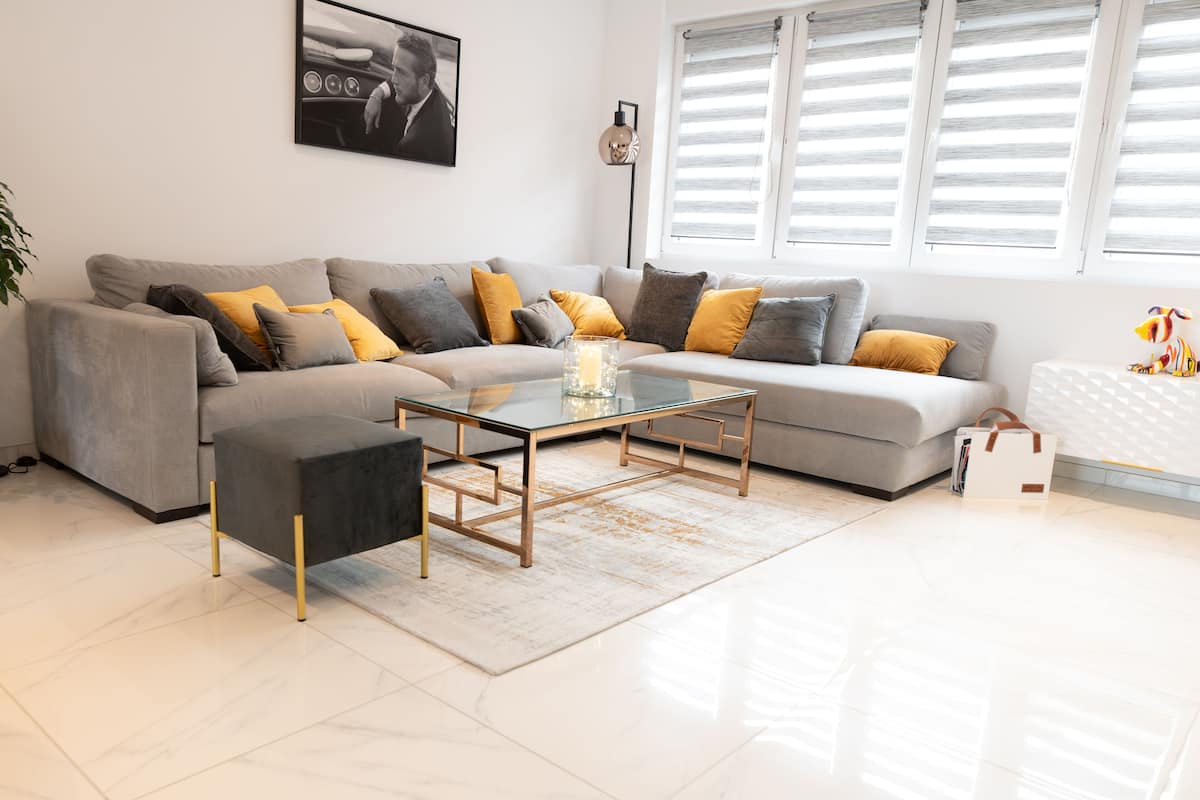 A modern living room with a grey sofa, a glass coffee table, and a white radiator.