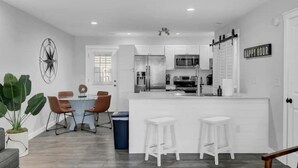 A modern kitchen with white cabinetry, a central island with stools, and a dining area with chairs.