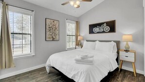 A bedroom with a large bed, two bedside tables with lamps, a ceiling fan, and artwork on the walls.