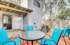 A covered patio with a round table and blue chairs, wooden deck, and a wooden fence.