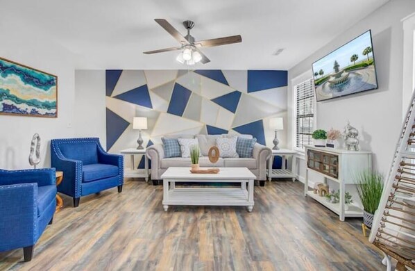 A modern living room with a geometric wall design, a ceiling fan, and a television mounted on the wall.