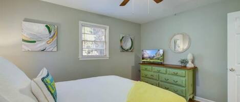 Une chambre à coucher avec un lit, un ventilateur de plafond, une commode verte et des œuvres d’art accrochées aux murs.
