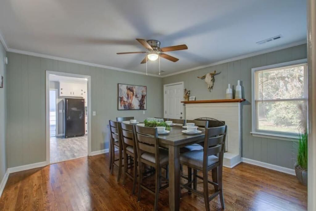A dining area with a wooden table and chairs, a ceiling fan, and a window with blinds.