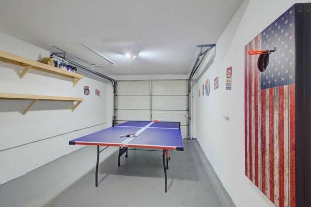 A ping pong table in a room with white walls, a ceiling fan, and a mural of the American flag.