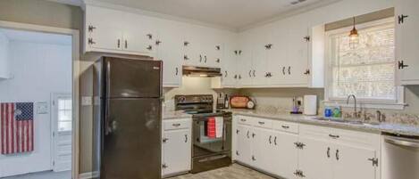 A kitchen with white cabinets, a stainless steel refrigerator, a built-in oven, and a window with blinds.