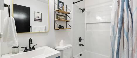 Un baño con lavamanos blanco, grifo negro, inodoro blanco y ducha con puerta de cristal.