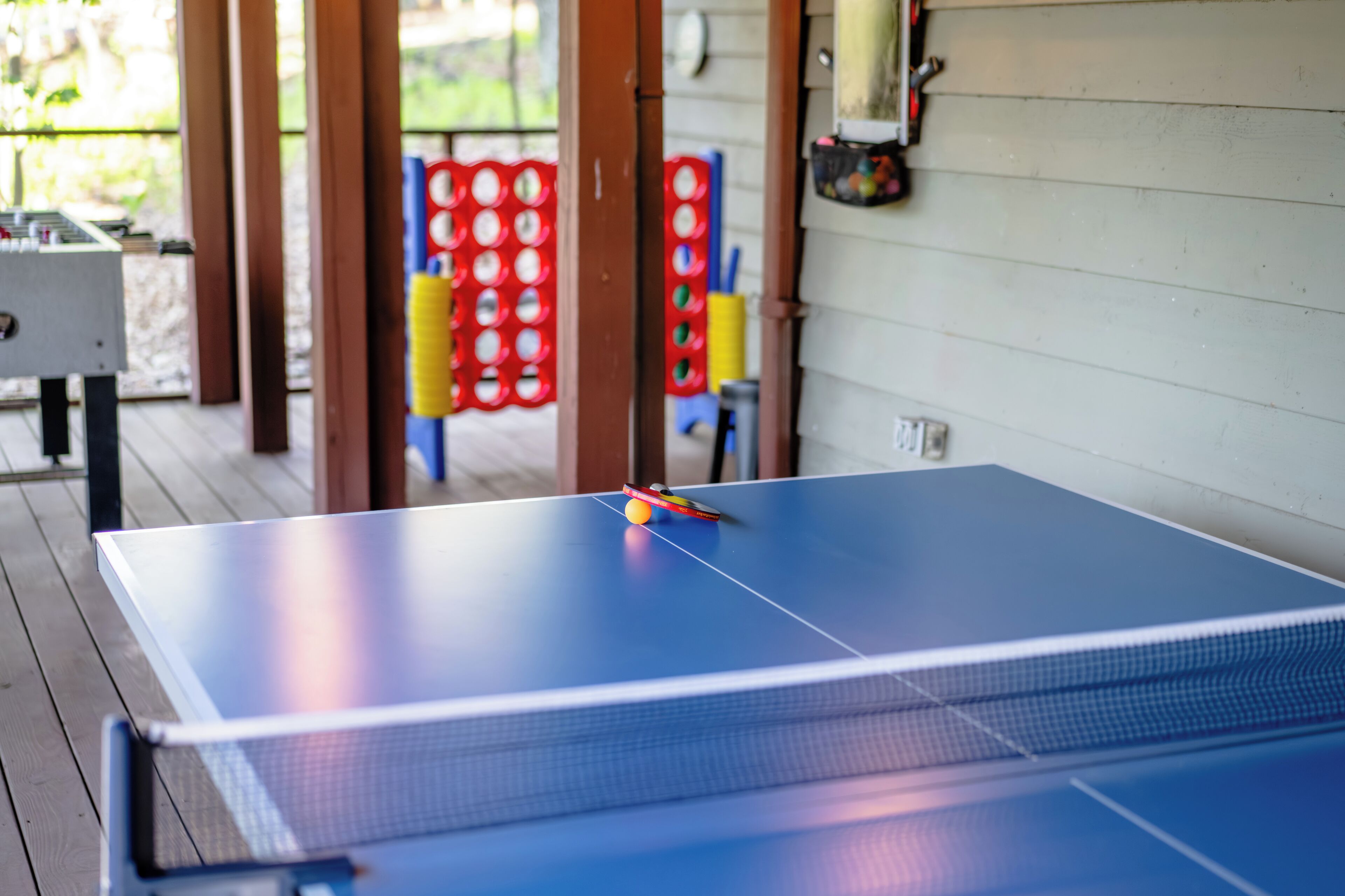 Een tafeltennistafel met bal en racket, een tafelvoetbaltafel, en een rode en gele speelconstructie op de achtergrond.