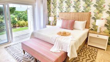 A bedroom with a large bed, a bench, a nightstand, and a view of greenery through a sliding door.