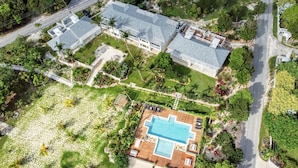 Eine Vogelperspektive zeigt einen Ferienort mit einem großen Swimmingpool, mehreren Gästevillen und üppiger Bepflanzung.