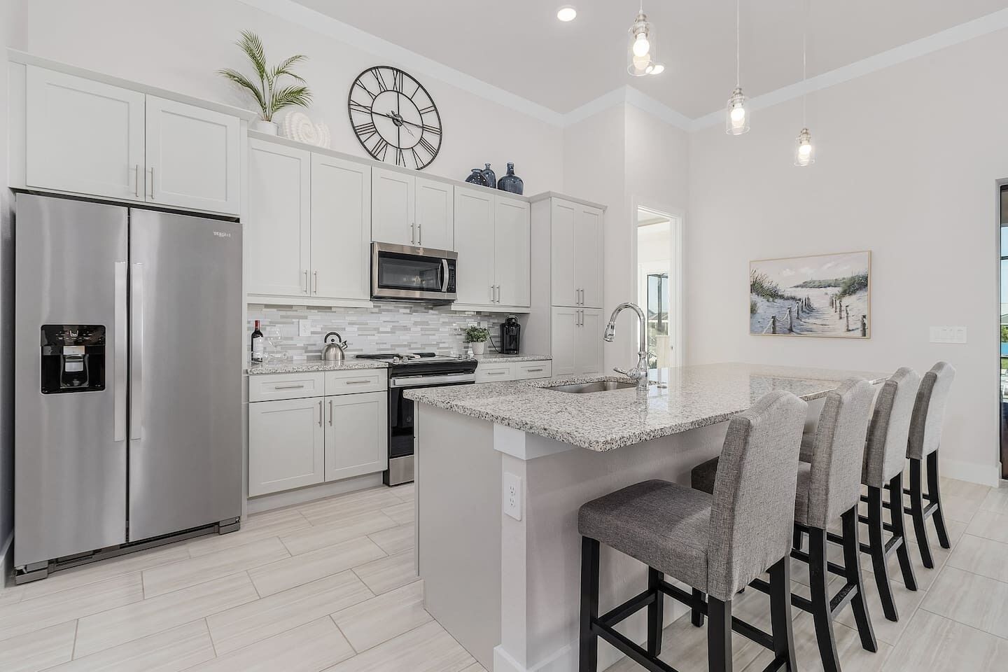A modern kitchen with white cabinetry, stainless steel appliances, a central island with bar stools, and a clock on the wall.