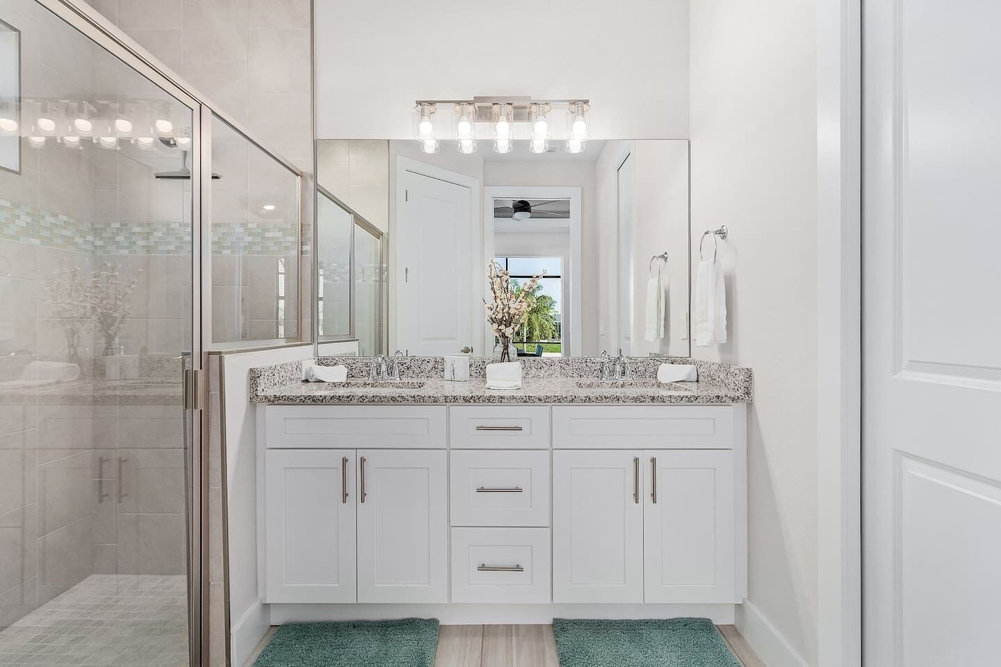 A modern bathroom with a granite countertop, white cabinetry, and a large mirror.