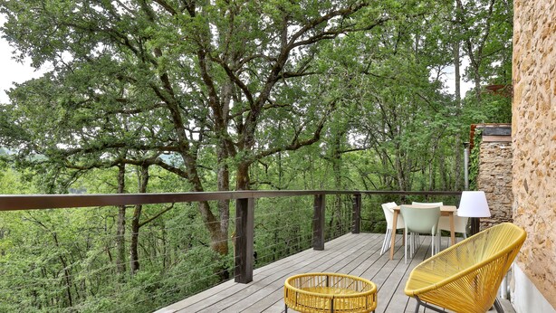 Terraza de madera con una silla de mimbre y una mesa, con vistas a un área boscosa.