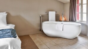 Un baño moderno con una bañera independiente, un radiador y una ventana con cortinas.