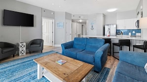 A modern living room with a blue sofa, a wooden coffee table, and a flat-screen TV. - 9th-Floor Gulf Sunset Views | 2 King Beds | Shores of Panama 920 (Panama City Beach)