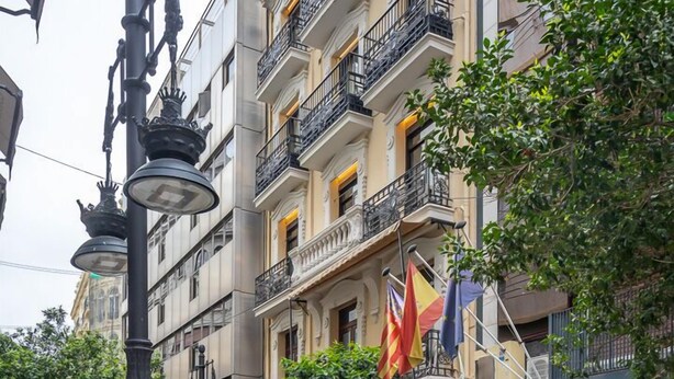 A multi-story building with balconies, a street lamp, and flags. - Nommadas Jero Hotel - Adults Only (Valencia)