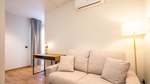 A modern living room with a beige sofa, a wooden desk, and a standing lamp. - Nommadas Jero Hotel - Adults Only (Valencia)