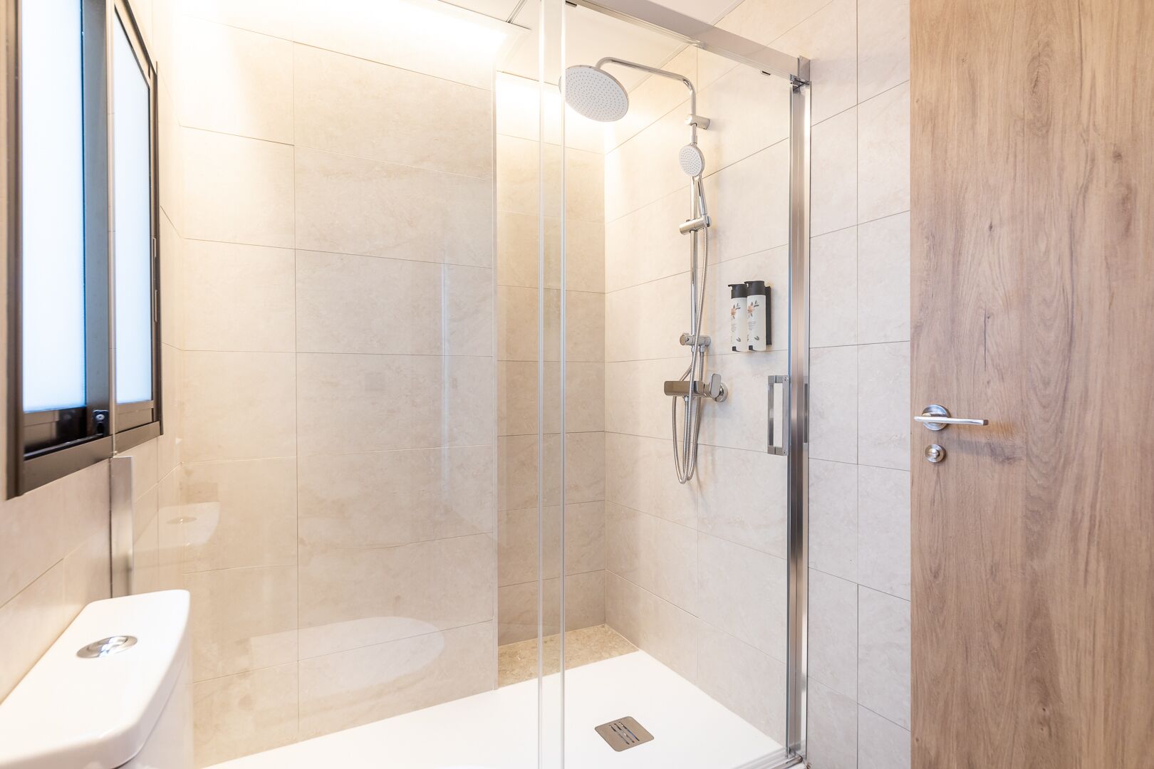 A modern bathroom with a glass-enclosed shower, a toilet, and a wooden door.