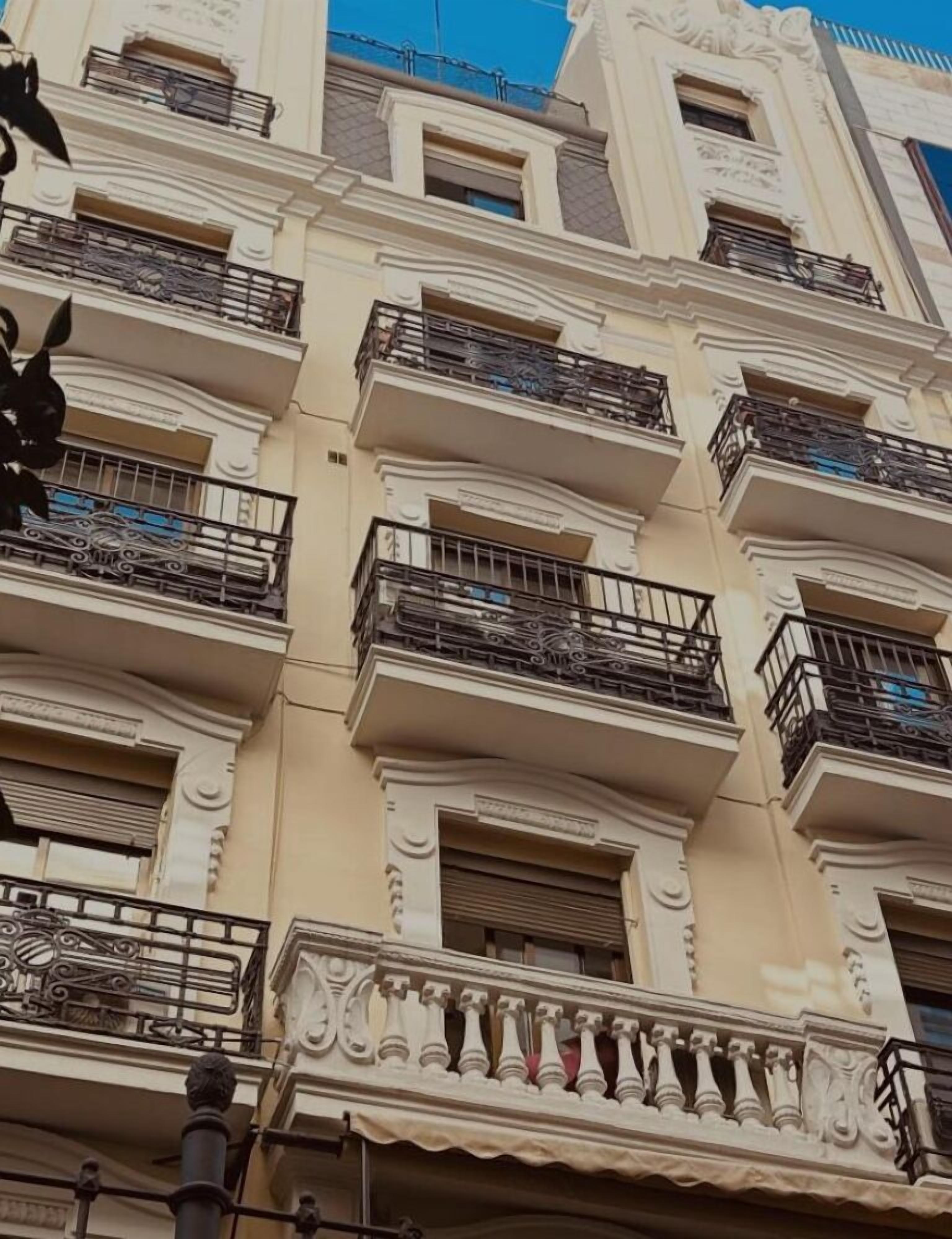 Un edificio de varios pisos con balcones, detalles arquitectónicos ornamentales y un cielo azul despejado.